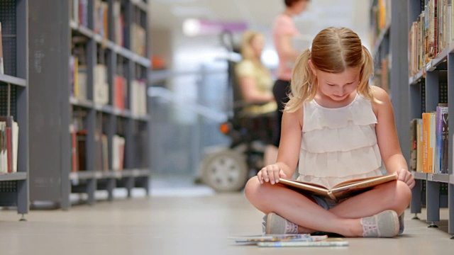 一个女孩坐在公共图书馆的书架旁看书视频素材
