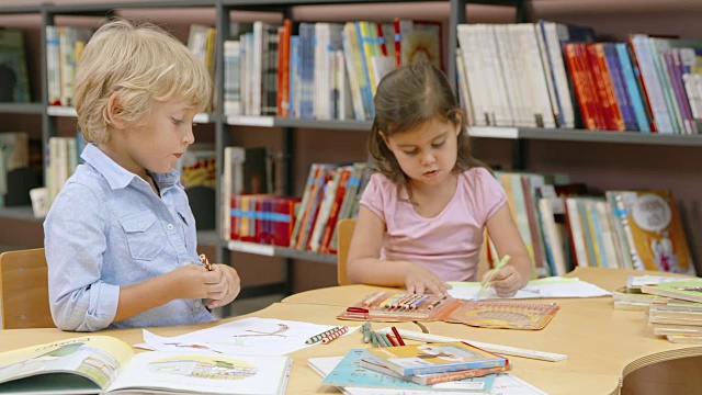 男孩和女孩坐在图书馆里用彩色铅笔画画视频下载