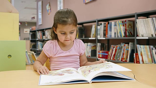 一个小女孩在公共图书馆的儿童桌旁看书视频素材