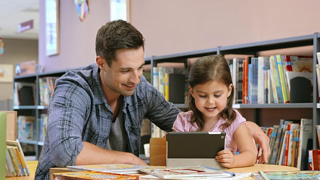 在公共图书馆里，爸爸看着女儿使用平板电脑视频素材