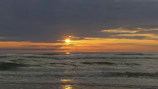 T/L橙色的太阳上升到海洋上方的云，背光的波浪，反射在前景视频下载