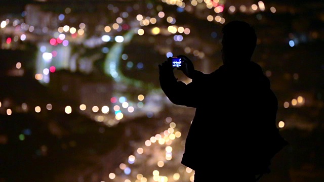 一个旅行者的剪影观光巴塞罗那城市夜间从高架视点与智能手机拍摄的巴塞罗那城市景观照片。视频素材