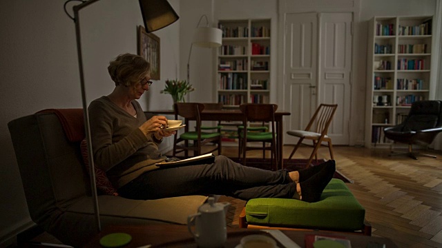 一位迷人的老妇人正舒服地躺在沙发上，享受着一杯热茶视频素材