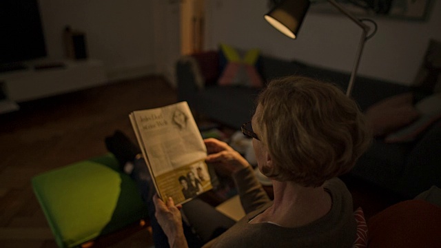 一位迷人的资深女士正舒服地躺在沙发上看报纸视频素材