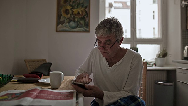 一位精力充沛的老人一边喝着咖啡，一边在用他的智能手机打字视频下载