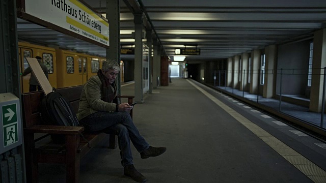一位精力充沛的老人在柏林地铁站等车，一边打字一边打手机视频下载