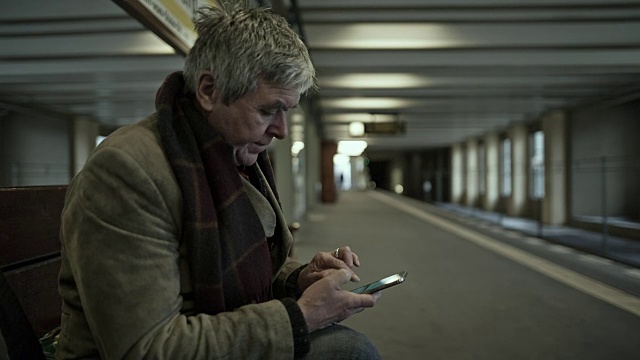 一位精力充沛的老人在柏林地铁站等车，一边打字一边打手机视频下载