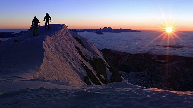 日落时分，两个人穿着雪鞋越过山脊视频素材