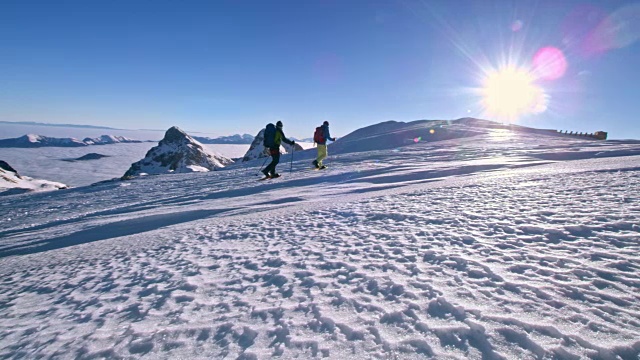 两个男人在阳光下穿雪鞋越过一座山视频素材