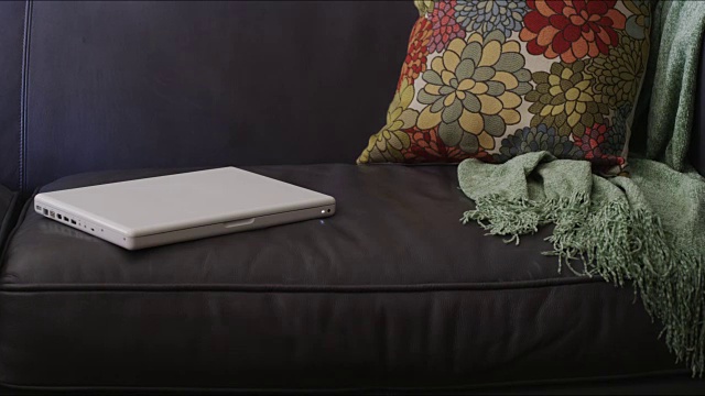 年轻女孩坐在沙发上用白色笔记本电脑的图片;她合上盖子，走出画框。视频下载
