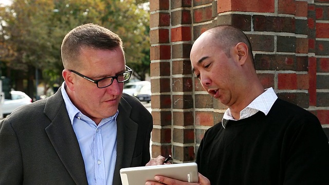 图为两名男子站在平板电脑上签署电子签名，随后握手/美国加州圣克鲁斯视频素材