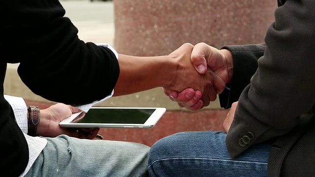 美国加州圣克鲁斯，一名男子坐在那里，将平板电脑递给另一名男子，让他签署电子签名，然后握手视频素材