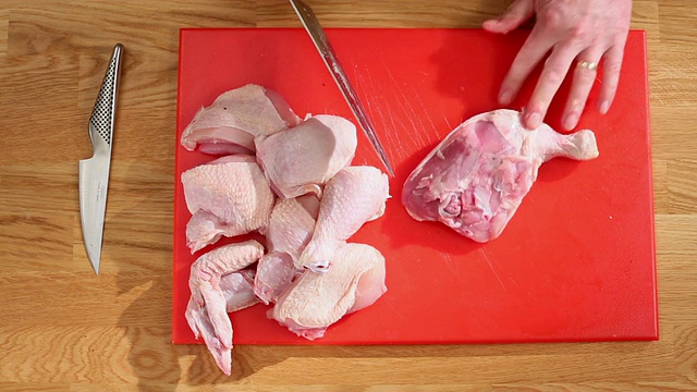 女士的厨师生鸡肉切成零件分开大腿腿红切菜板/新港,英国南威尔士aE视频素材