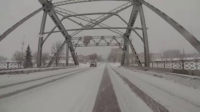 在一个阴沉沉的冬日里，开车穿过一座古老的铁桥，进入一个下雪的中西部市区。视频下载