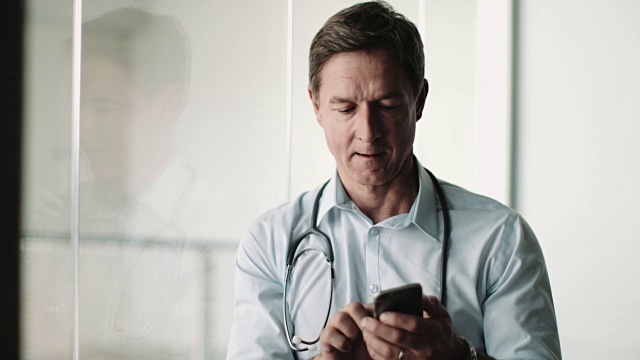 在医院使用智能手机的成年男性医生视频素材