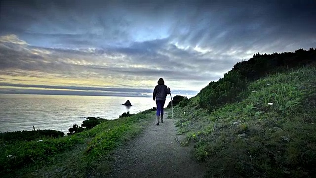 成熟的中年妇女徒步在海边的日落小径视频下载
