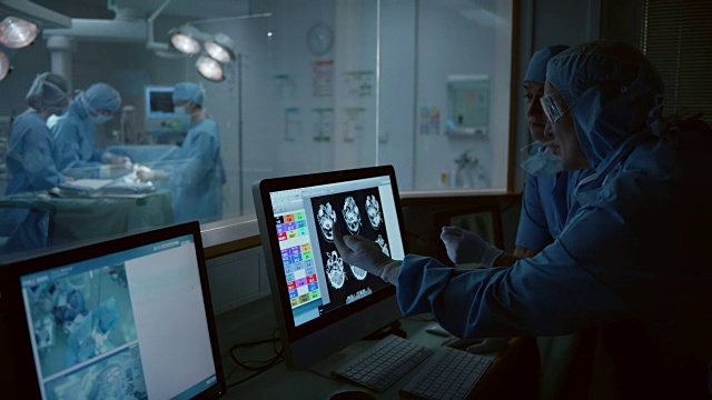 女外科医生和她的助手在手术室旁边讨论头部扫描视频购买