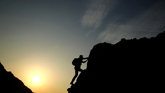 夕阳下男性攀登者的剪影。视频下载