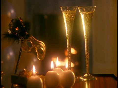从近距离缩小香槟被倒进两个杯子上的蜡烛+面具/壁炉的背景视频素材