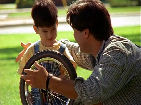 慢动作年轻的西班牙男孩帮助男人把车轮放在户外的自行车上/男人拥抱+亲吻他视频素材