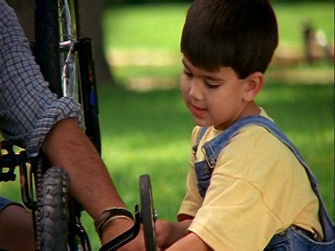 慢镜头西班牙男子帮助小男孩在户外用扳手拧紧自行车上的螺栓视频素材