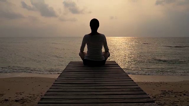 日落时分，在海滩海边的木桥上练习瑜伽的女人，4k(超高清)视频下载