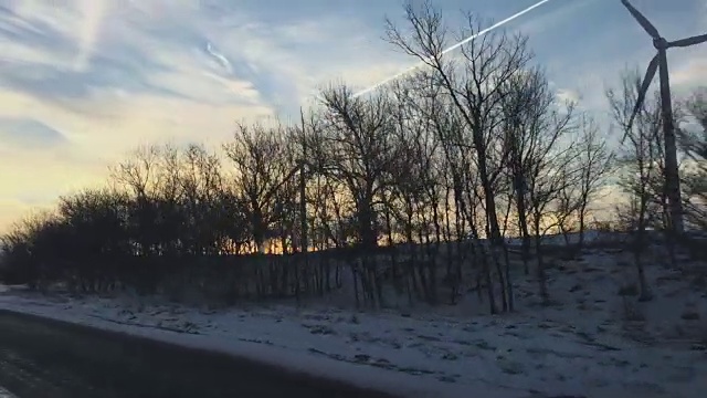 当太阳升起的时候，一辆汽车的挡风玻璃在高速公路上飞驰而过，乡间的冬季景色中有许多空气涡轮发电机在生产清洁能源视频下载