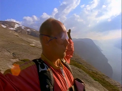 特写:男性跳伞者戴着护目镜和连体衣伸展在悬崖的边缘/瑞典视频素材