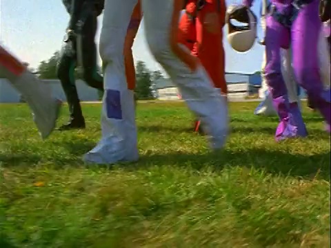 低角度侧面的视角跳伞运动员穿着五颜六色的工作服，带着头盔在草地上慢跑经过摄像机视频下载