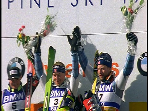 慢镜头放大SWISH pan速降滑雪获胜者站在平台上，双手高举在人群面前视频下载