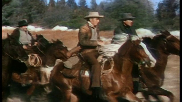 19世纪60年代，一群牛仔骑着骏马在平原上奔跑，站在队伍前面的是伦道夫·斯科特(戴着浅棕色的帽子，穿着棕色的外套)和福雷斯特·塔克(戴着灰色的帽子，穿着深蓝色的外套)。视频素材
