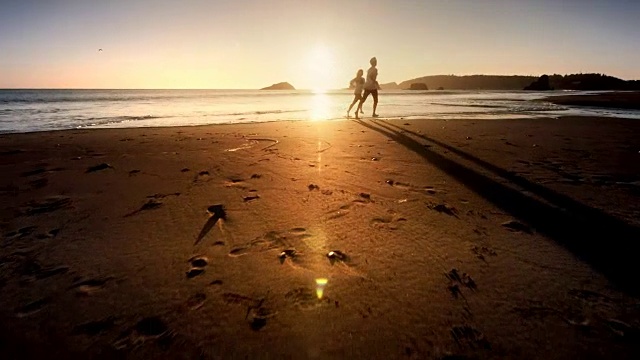 日落时分，一对年轻夫妇在太平洋海滩上跑步视频素材