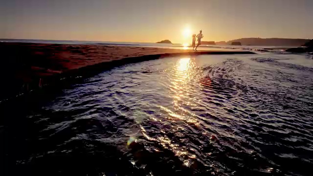 日落时分，一对年轻夫妇在太平洋海滩上跑步视频素材