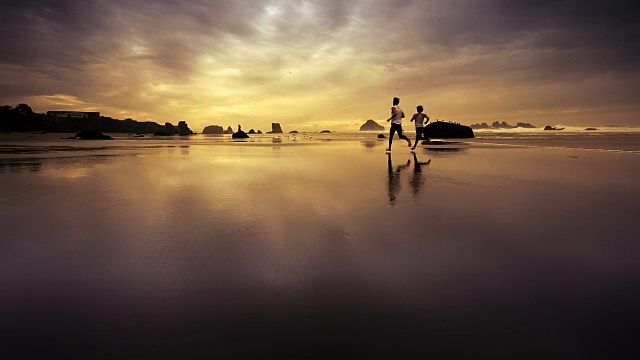 日落时分，一对年轻夫妇在海滩上慢跑视频素材