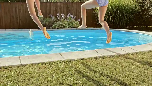 两个女孩在阳光下跳进游泳池视频素材