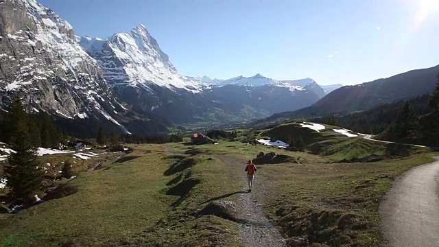 日出时，一名男性徒步者沿着山间草地下山视频素材