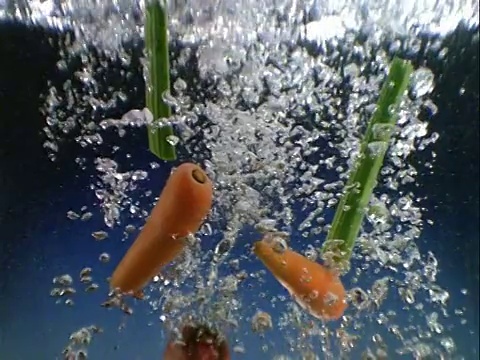 慢动作特写蔬菜掉进水里，以蓝色为背景视频素材