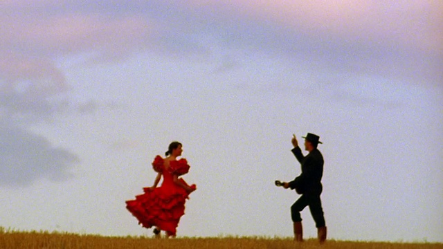 在西班牙平原上，身着红色弗拉门戈服装的女子与戴着帽子弹吉他的男子共舞视频下载