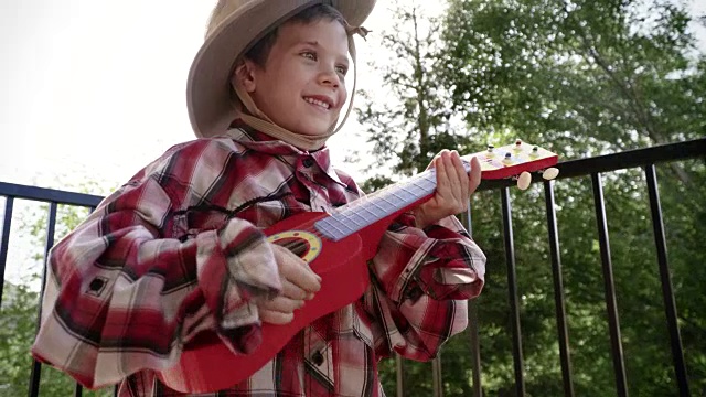4k小男孩穿着乡村衣服弹奏尤克里里琴视频素材