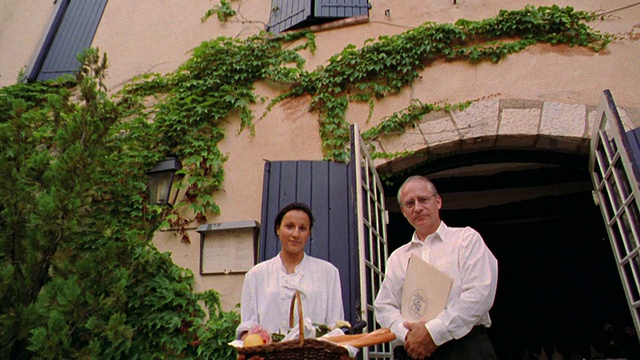 低角度拍摄倾斜下来的男人拿着菜单+女人拿着食物篮子站在餐厅/法国视频素材