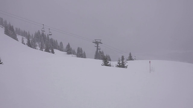 山上有雾，还在下雪。空的升降椅在底部运行。视频下载