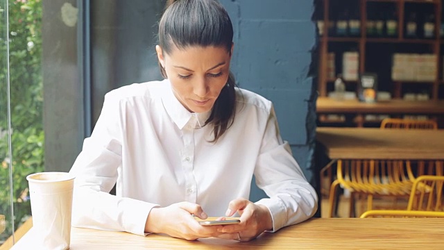 一名年轻女子在咖啡店里使用智能手机。视频素材