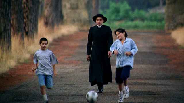 神父+两个男孩在意大利的乡村道路上对着摄像机跑+踢足球视频下载