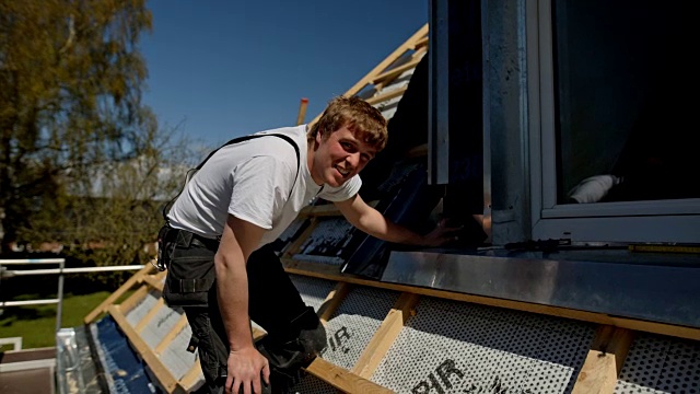 一个年轻的屋顶工人在一个新建的房子的屋顶上工作的肖像视频下载