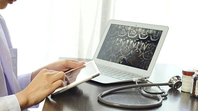女性医生在平板电脑上检查图像x射线核磁共振，笔记本电脑和药瓶视频下载
