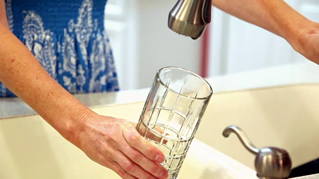 女人可以喝到装在玻璃杯里的清水。厨房的水槽。视频素材