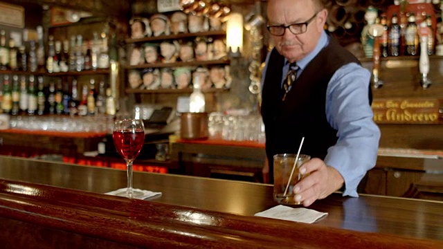 MS高级调酒师把威士忌加冰鸡尾酒旁边的一杯玫瑰葡萄酒视频下载