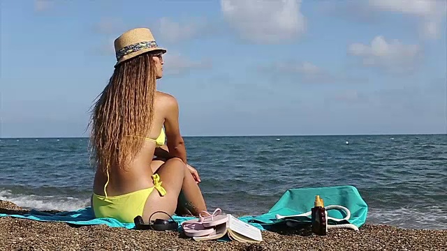 性感的女人在夏天的帽子和比基尼坐在海滩上视频素材