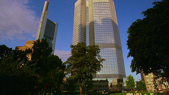 低角度倾斜向上倾斜摩天大楼(德国商业银行大厦+欧洲大厦)，在前景公园树木/德国法兰克福视频下载