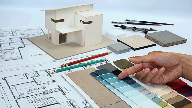 建筑师和室内设计师工作在工作台上与家庭模型，蓝图，织物样品视频下载